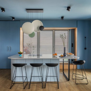 Interior design of kitchen space with marble island, black chockers, modern lamp, wooden wall, blue kitchen furnitures, vase with dried flowers and personal accessories. Home decor. Template. 