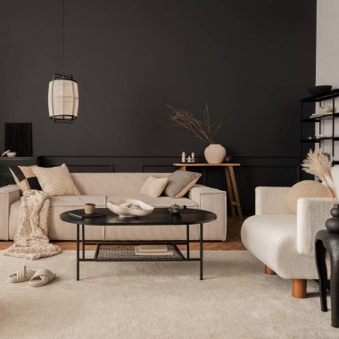 Creative composition of living room interior with modular beige sofa, black coffee table, armchair, rug, black wall with stucco, vase with dried flowers and personal accessories. Home decor. Template.