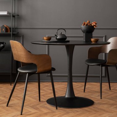 Minimalist composition of living room interior with black round coffee table, stylish chair, wooden sideboard, dark wall with stucco, pitcher, lamp and personal accessories. Home decor. Template.