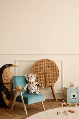 Mavi koltuk, peluş oyuncaklar, ahşap bloklar, ahşap büfe, bej duvarlı sıva, örülmüş penguen ve kişisel aksesuarlarla çocuk odasının minimalist kompozisyonu. Ev dekoru. Şablon.