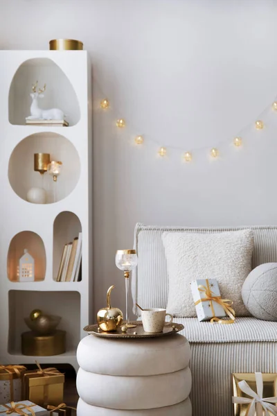 Amazing composition on white design shelf with christmas decoration, lights, gifts, lanterns ,deer, candles, stars, white corduroy sofa and pouf. Santa claus is coming. Home decor. Template.
