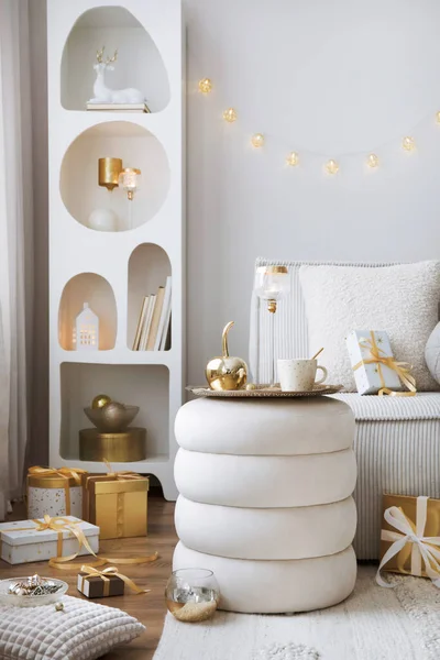 Amazing composition on white design shelf with christmas decoration, lights, gifts, lanterns ,deer, candles, stars, white corduroy sofa and pouf. Santa claus is coming. Home decor. Template.