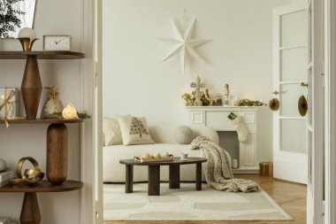 Krem rengi kanepe ve çelenkli şömine rafı, ışıklar ve tatil figürleri. Tatil sezonu için sıcak, rahat bir ortam..