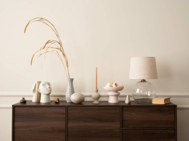 Ahşap büfe, cam lamba, kurumuş çiçekli vazo, modern heykel, kitaplar, sıva ve kişisel aksesuarlarla dolu duvar ile oturma odasının estetik yapısı. Ev dekoru. Şablon.