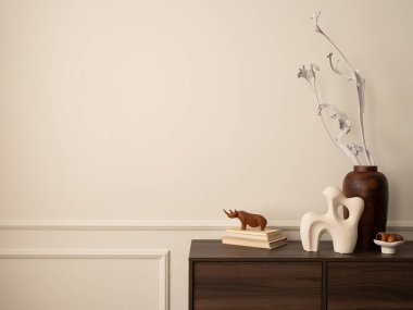 Ahşap büfe, cam lamba, kurumuş çiçekli vazo, modern heykel, kitaplar, sıva ve kişisel aksesuarlarla dolu duvar ile oturma odasının estetik yapısı. Ev dekoru. Şablon.