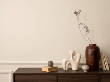 Ahşap büfe, cam lamba, kurumuş çiçekli vazo, modern heykel, kitaplar, sıva ve kişisel aksesuarlarla dolu duvar ile oturma odasının estetik yapısı. Ev dekoru. Şablon.