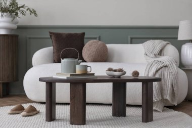 Oturma odasının içinde küçük kanepe, ahşap sehpa, şık büfe, kahverengi yastıklar, bej ekose, terlikler, yuvarlak halı ve kişisel aksesuarlar var. Ev dekoru. Şablon.