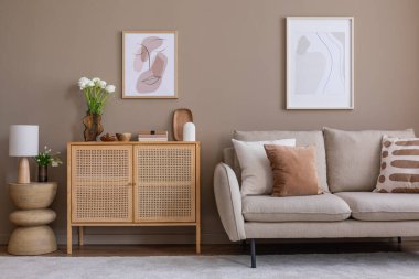 Rahat ve sıcak oturma odasının iç tasarımı poster çerçevesi, rattan büfe, bej kanepe, kahverengi yastık, kurumuş çiçekli vazo, heykel ve kişisel aksesuarlar. Ev dekoru. Şablon. 