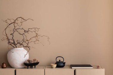 Oturma odasının minimalist kompozisyonu fotokopi alanı, basit bej büfe, dallı vazo, kitaplar, şık siyah sürahi ve kişisel aksesuarlar. Ev dekoru. Şablon.