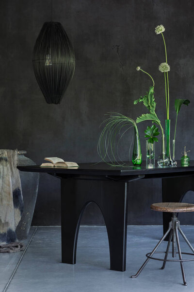 Минималистская композиция интерьера столовой джапанди с черным столом, стеклянная ваза с зелеными цветами, разбрызгиватель, клетчатый, кресло, бетонная стена и личные аксессуары. Интерьер дома. Шаблон.