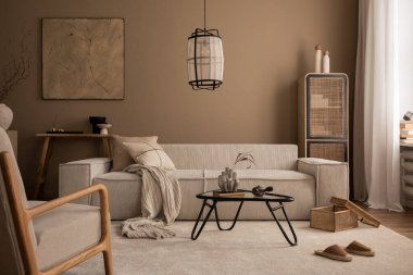 Poster çerçevesi, bej kanepe, cam sehpa, bej duvar, puf, rattan büfe, terlik, ahşap bank ve kişisel aksesuarları olan oturma odasının iç tasarımı. Ev dekoru.