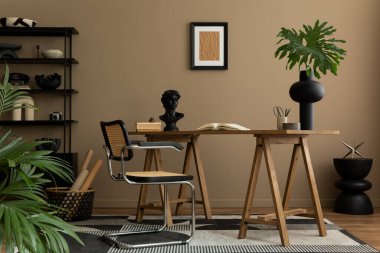 Poster çerçevesi, ahşap masa, rattan sandalye, siyah raf, desenli halı, bitki, kahverengi duvar, kitaplar ve kişisel aksesuarlarla birlikte yaratıcı bir iç mimari. Ev dekoru. Şablon.