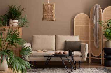 Sıcak ve rahat oturma odasının iç tasarımı bej kanepe, boho lambası, ahşap bölme duvarı, yastık, cam sehpa, saksıda bitkiler ve kişisel aksesuarlar. Ev dekoru. Şablon