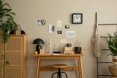 Poster çerçevesi, ahşap masa, ahşap büfe, sandalye, saksıdaki bitkiler, siyah merdiven, kalem ve kişisel aksesuarlarla donatılmış yaratıcı ofis içeriği. Ev dekoru. Şablon.