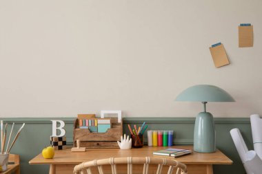 Ahşap masa, koltuk, nane lambası, kitaplar, şık heykeller, kalemler, sıva ve kişisel aksesuarlarla bej ve yeşil duvarlı samimi ofis iç mimarisi. Ev dekoru. Şablon.