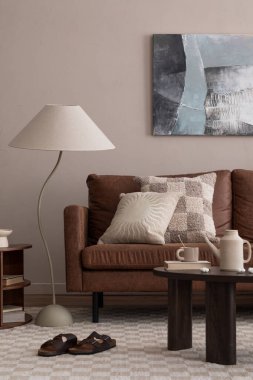 Poster çerçevesi, kahverengi kanepe, ahşap sehpa, bej sürahi, şık lamba ve kişisel aksesuarları olan yaratıcı bir oturma odası kompozisyonu. Ev dekoru. Şablon.