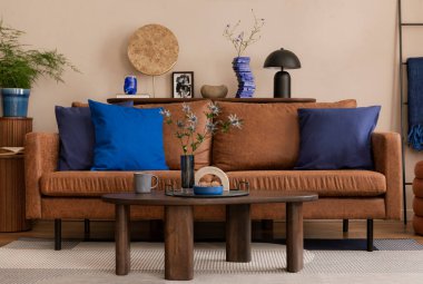 Kahverengi kanepe, mavi yastıklar, ahşap sehpa, şık bir lamba, kurumuş çiçekler ve kişisel aksesuarlı vazo ile oturma odasının yaratıcı kompozisyonu. Ev dekoru. Şablon.