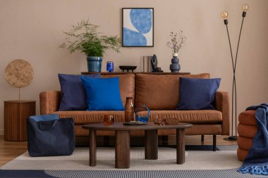 Poster çerçevesi, kahverengi kanepe, ahşap sehpa, şık lamba, bitkiler, perde, bej duvar ve kişisel aksesuarlarla dekore edilmiş şık bir oturma odası kompozisyonu. Ev dekoru. Şablon.