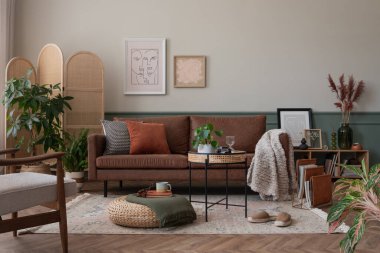 Poster çerçevesi, kahverengi kanepe, ahşap bölme duvarı, bej halı, bitkiler ve kişisel aksesuarlarla dolu sıcak ve rahat oturma odasının yaratıcı kompozisyonu. Ev dekoru. Şablon.