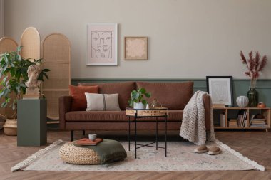 Poster çerçevesi, kahverengi kanepe, ahşap bölme duvarı, bej halı, bitkiler ve kişisel aksesuarlarla dolu sıcak ve rahat oturma odasının yaratıcı kompozisyonu. Ev dekoru. Şablon.