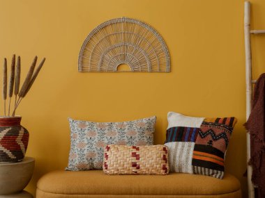 Sıcak oturma odasının iç tasarımı şık bank, desenli yastıklar, sarı duvar, duvarda süs, siyah raf, kurumuş çiçekler ve kişisel aksesuarlarla dolu vazo. Ev dekoru. Şablon.