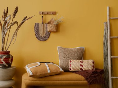 Sıcak oturma odasının iç tasarımı şık bank, desenli yastıklar, sarı duvar, duvarda süs, siyah raf, kurumuş çiçekler ve kişisel aksesuarlarla dolu vazo. Ev dekoru. Şablon.