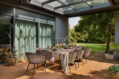 Büyük masalı, bahçe sandalyeli, ekoseli, saksılı, masa örtülü, meyveli, çörekli, kahverengi masa örtülü ve kişisel aksesuarlı güzel bir teras kompozisyonu. Ev dekoru. Şablon.