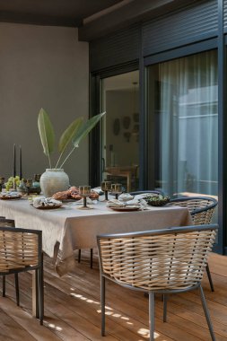 Terasın iç tasarımı bahçe koltuğu, yastıklar, çiçekli vazo örülmüş sepet, ekose, büyük pencere, kase, ahşap zemin ve kişisel aksesuarlarla. Ev dekoru. Şablon.