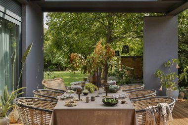 Masa, bahçe mobilyaları, çiçekli vazo, ahşap döşeme, ekose, perde, üzüm, büyük bahçe ve kişisel aksesuarlı yaratıcı kompozisyon. Ev dekoru. Şablon.