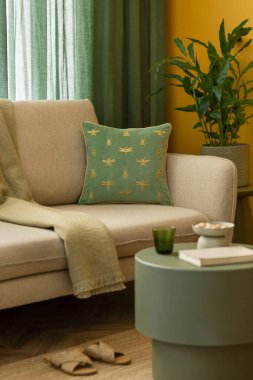 Sarı duvar, bej kanepe, yeşil sehpa, ekose, terlik, kitaplar, cam bardak, fındık, örülmüş halı ve kişisel aksesuarlarla oturma odasının yaratıcı bileşimi. Ev dekoru. Şablon.