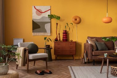 Ahşap büfe, sehpa, kahverengi kanepe, sarı duvar, kilim kilim halı, turuncu lamba, yapraklı vazo ve kişisel aksesuarları olan yaratıcı bir kompozisyon. Ev dekoru. Şablon.