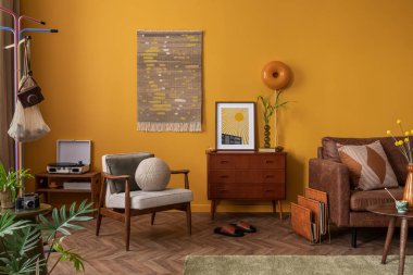 Ahşap büfe, sehpa, kahverengi kanepe, sarı duvar, kilim kilim halı, turuncu lamba, yapraklı vazo ve kişisel aksesuarları olan yaratıcı bir kompozisyon. Ev dekoru. Şablon. 