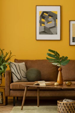 Sarı oturma odasının iç tasarımı poster çerçevesi, kahverengi kanepe, ahşap sehpa, terlik, yeşil halı, sepet, turuncu lamba ve kişisel aksesuarlar. Ev dekoru. Şablon.