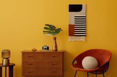 Antika oturma odasının iç dekorasyonunda şablonlu killim halı, kırmızı koltuk, şık ahşap büfe, bordo tabure, sarı duvar ve kişisel aksesuarlarla minimalist kompozisyon. Ev dekoru. Şablon.