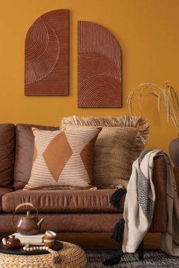 Sıcak ve rahat oturma odasının iç tasarımı kahverengi kanepe, sarı duvar, örülmüş puf, yapraklı vazo, kitaplar, desenli halı ve kişisel aksesuarlarla. Ev dekoru. Şablon.