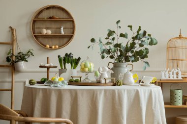 Warm and spring dining room interior with easter accessories, shelf on wall, round table, vase with green leaves, colorful eggs, rabbit sculpture and personal accessories. Home decor. Template.
