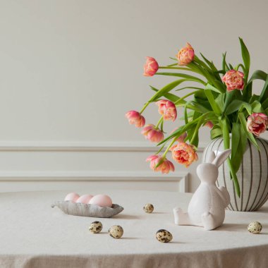Minimalist composition of easter dining room interior with copy space, vase with tulips, colorful eggs, gray hen sculpture, beige wall with stucco and personal accessories. Home decor. Template.