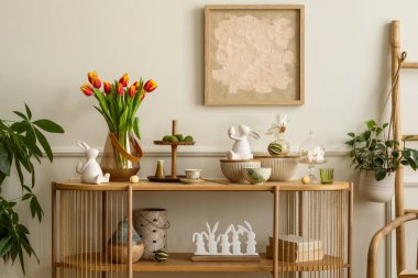 Interior design of easter living room interior with mock up poster frame, glass vase with tulips, wooden sideboard, easter bunny sculpture, bowl, ladder, and personal accessories. Home decor. Template