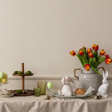 Creative composition of easter living room interior with copy space, vase with spring tulips, easter bunny sculpture, elegant cup, colorful easter eggs and personal accessories. Home decor. Template.