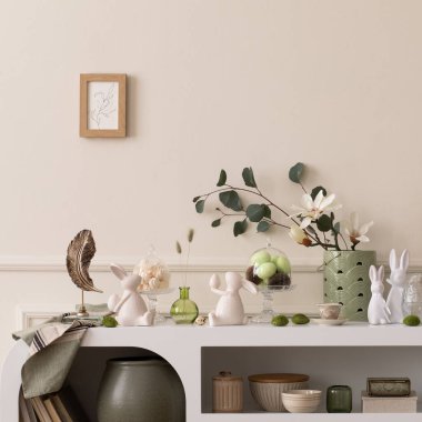 Interior design of easter living room interior stylish sideboard, colorful easter eggs, easter bunny sculpture, vase with leaves, magnolia and personal accessories Home decor. Template.