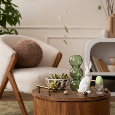 Aesthetic composition of easter living room interior with boucle armchair, round pillow, vase with leaves, easter bunny, coffee table, colorful eggs and personal accessories. Home decor. Template.