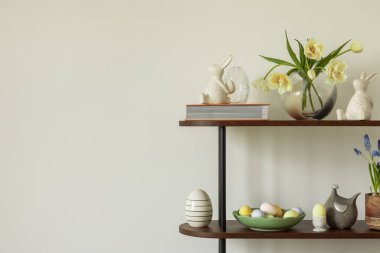 Tarafsız renk paleti olan Paskalya temalı bir oturma odası. Seramik tavşan heykelcikleri, pastel yumurtalar ve beyaz bir vazoda taze sarı lalelerle süslenmiş yuvarlak bir sedir, şenlikli bir dokunuş ekler..