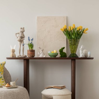 Tarafsız renk paleti olan Paskalya temalı bir oturma odası. Seramik tavşan heykelcikleri, pastel yumurtalar ve beyaz bir vazoda taze sarı lalelerle süslenmiş yuvarlak bir sedir, şenlikli bir dokunuş ekler..