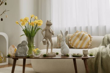 Samimi Paskalya temalı oturma odası. Tarafsız tonlar, sarı aksanlar ve dekoratif tavşanlar. Bahar çiçekleri, mumlar ve mevsimlik süsler sıcak bir tatil ortamı yaratır..