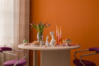 Modern ahşap bir masa, canlı laleler ve kalın turuncu bir duvara karşı yumuşak pastel süslemeler içeren minimalist Paskalya brunch düzeneği..