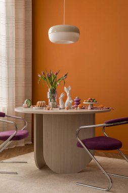 Minimalist Paskalya yemeği, çağdaş sandalyeler, yumuşak ışıklandırma ve ılık tonlu bir tatil düzenlemesi..