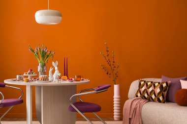 Pastel süslemeler, laleler, seramik tavşanlar ve sıcak turuncu bir duvara dayalı ahşap bir masa..