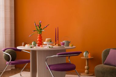 Pastel süslemeler, laleler, seramik tavşanlar ve sıcak turuncu bir duvara dayalı ahşap bir masa..