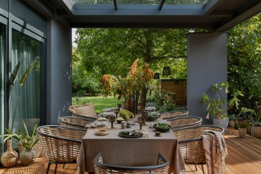 Masa, bahçe mobilyaları, çiçekli vazo, ahşap döşeme, ekose, perde, üzüm, büyük bahçe ve kişisel aksesuarlı yaratıcı kompozisyon. Ev dekoru. Şablon.