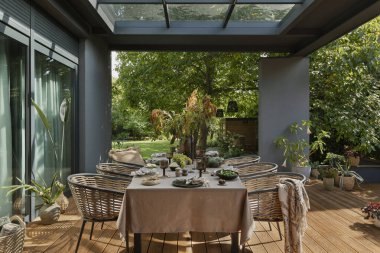 Masa, bahçe mobilyaları, çiçekli vazo, ahşap döşeme, ekose, perde, üzüm, büyük bahçe ve kişisel aksesuarlı yaratıcı kompozisyon. Ev dekoru. Şablon.